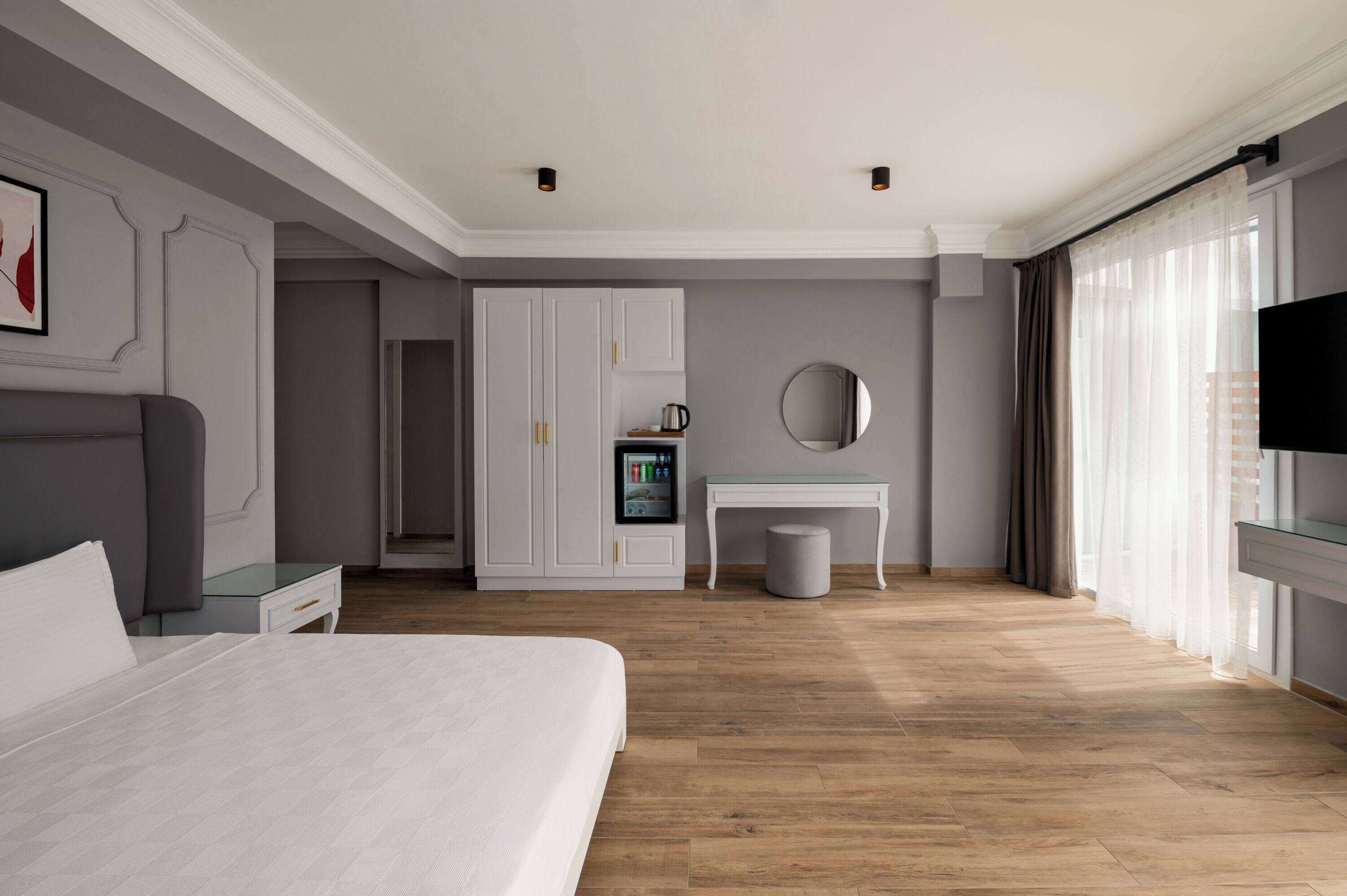 Quarto de hotel moderno com uma cama grande, uma toucador com espelho, uma mesa pequena e uma televisão.