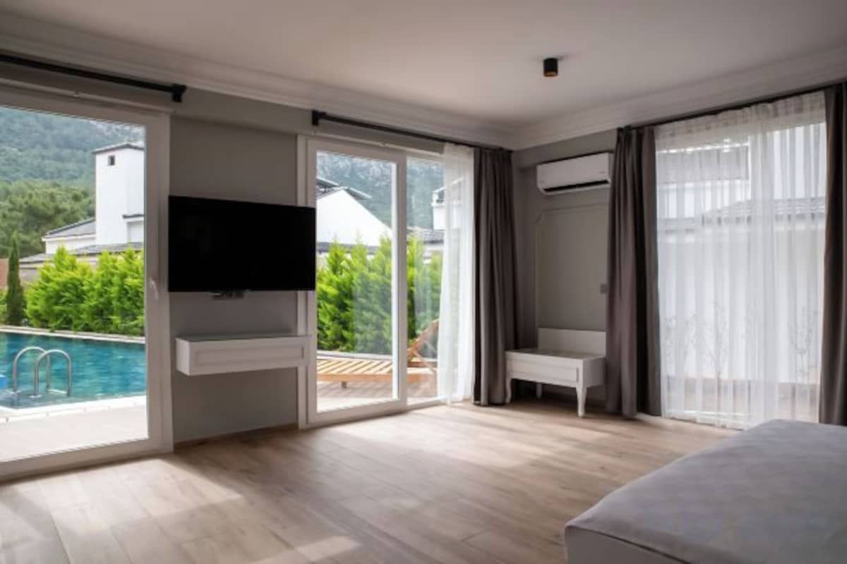 A modern hotel room with a large TV, a balcony with a pool, and a bed.