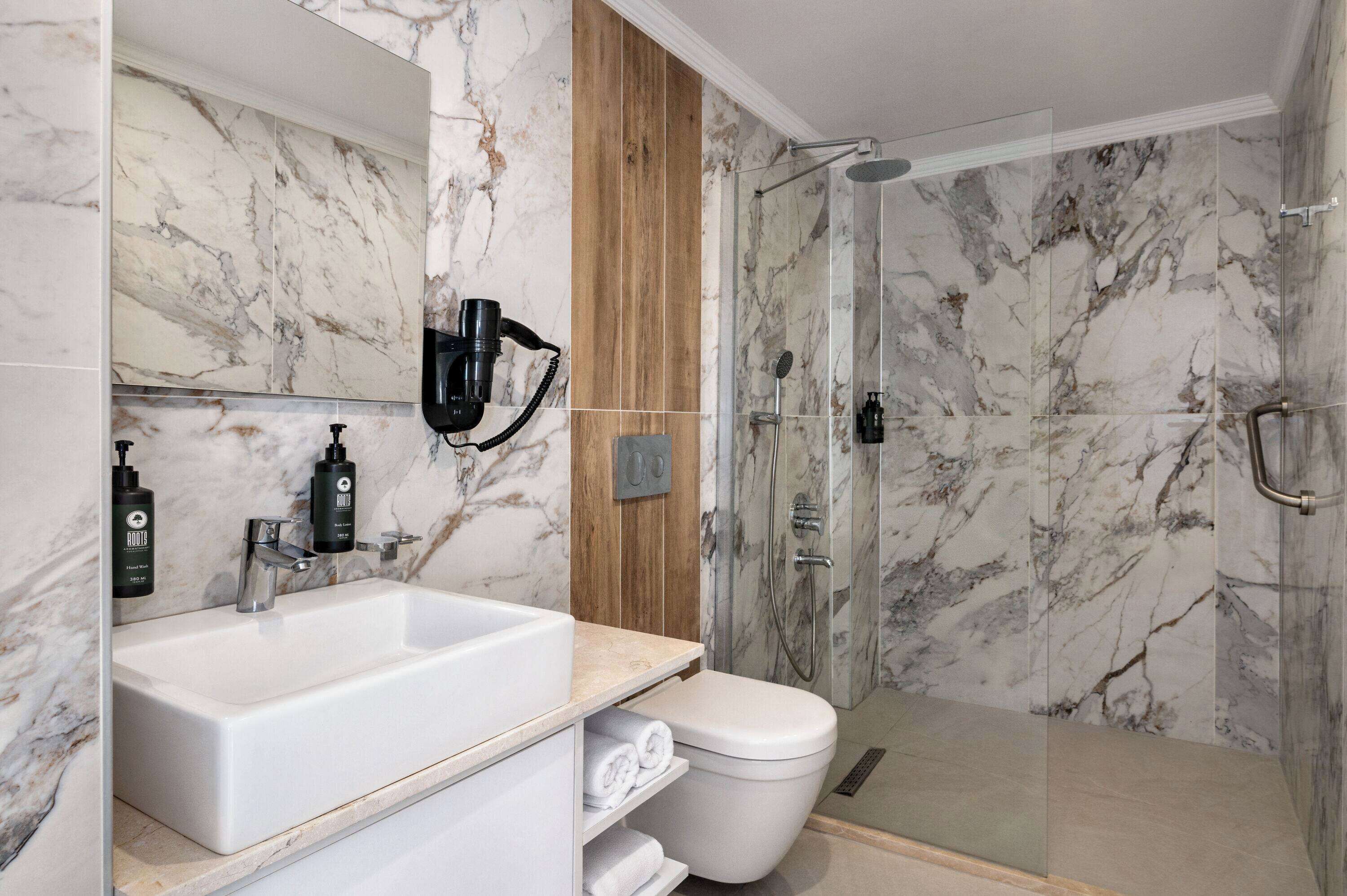 A modern bathroom with a marble sink, a toilet, and a glass-enclosed shower.