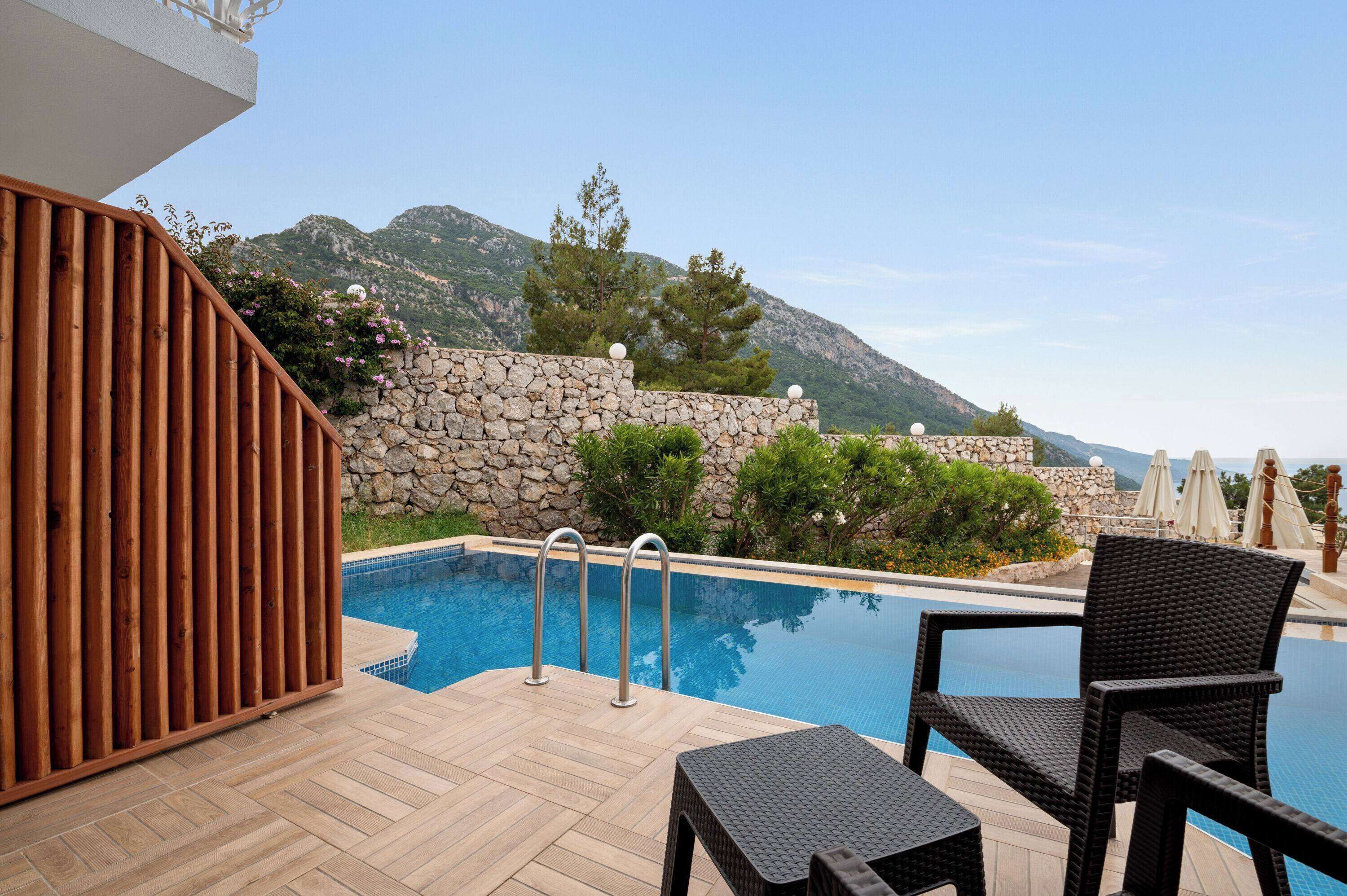 A pool area with a wooden deck, stone walls, and a view of mountains.