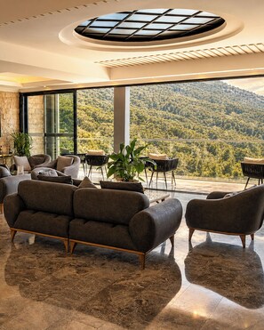 A modern living room with a large sofa, armchairs, and a coffee table. A large window offers a view of a forested mountain. - Ramada by Wyndham Fethiye Oludeniz (Fethiye)