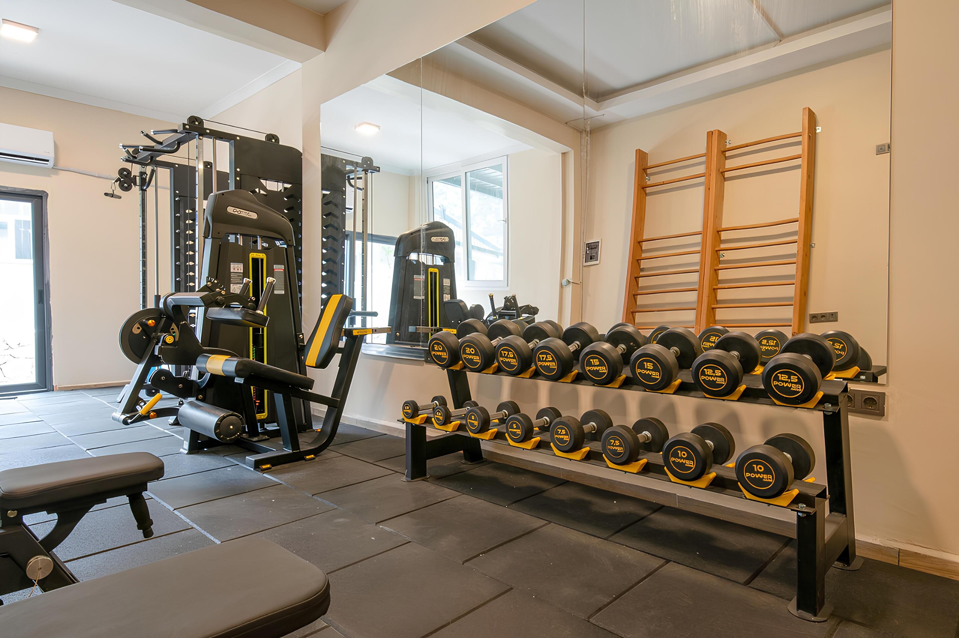 A gym with weightlifting equipment, dumbbells, and a bench.