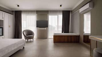 A modern hotel room with a bed, a chair, a large window with curtains, a flat-screen TV, a wooden bench, and an air conditioning unit.