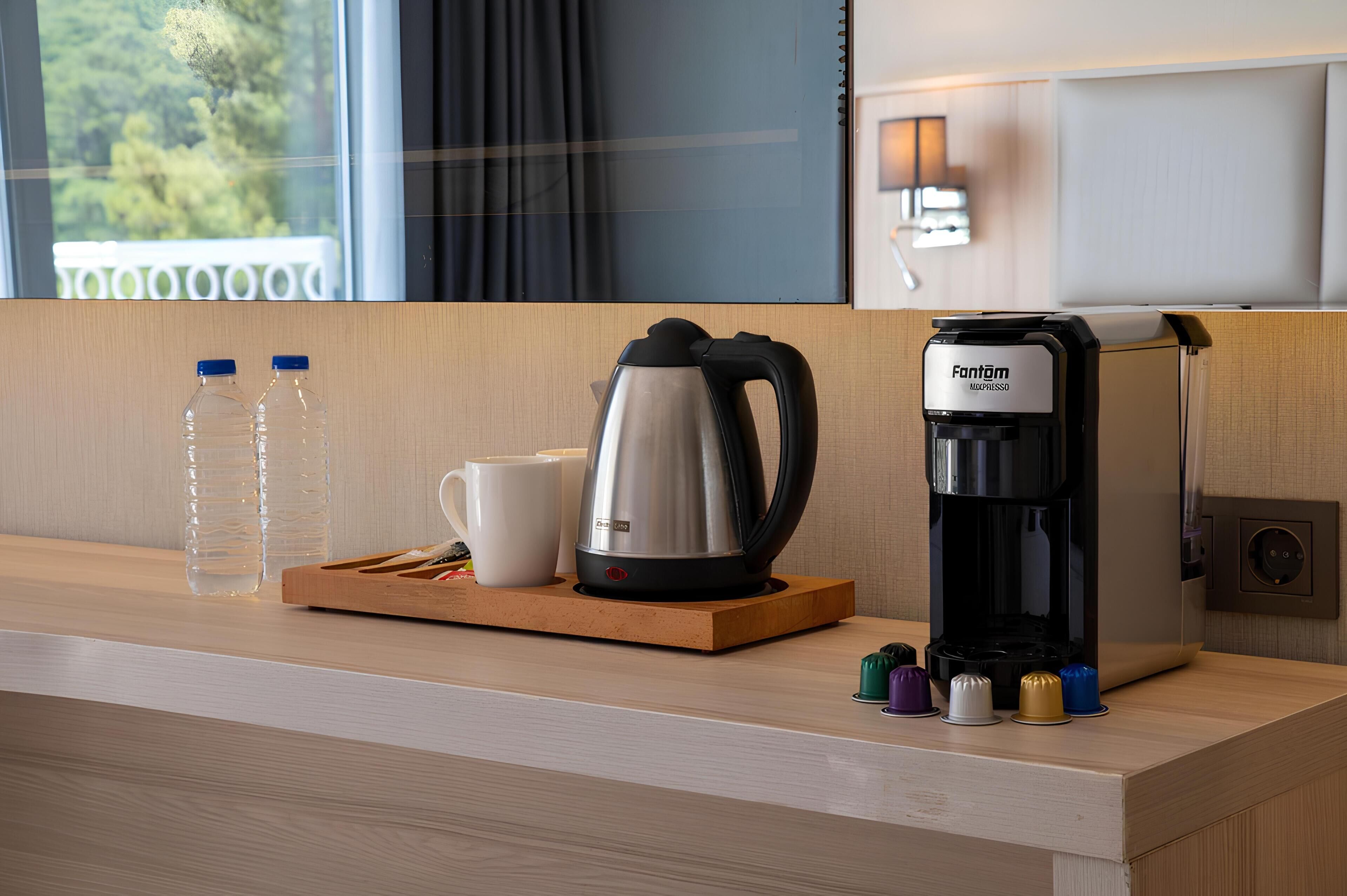 A hotel room's coffee station with a coffee maker, a kettle, a cup, and water bottles.