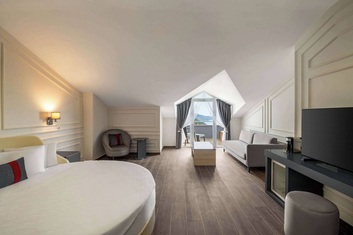 A hotel room with a large bed, a TV, a sofa, and a balcony with a view.