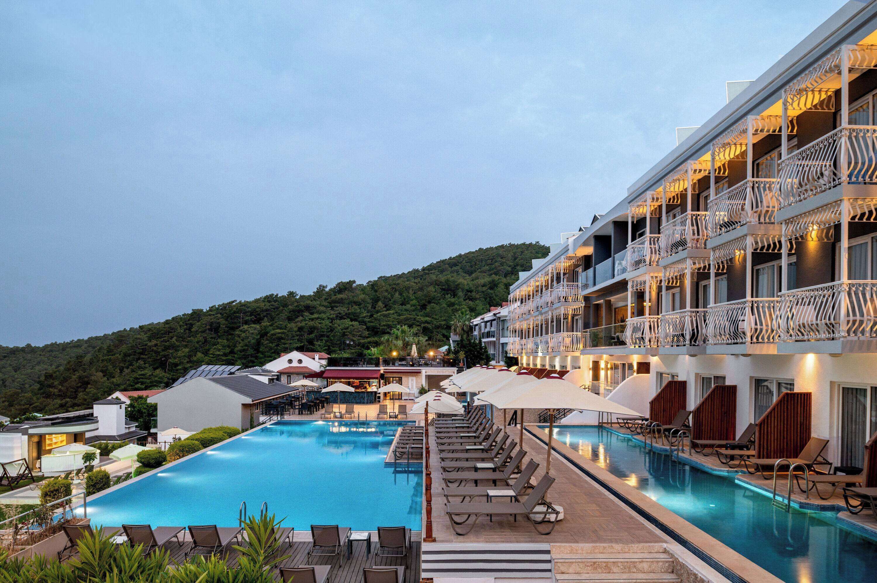 A hotel with a swimming pool, lounge chairs, and a view of the surrounding landscape.