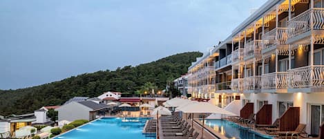 A hotel with a swimming pool, lounge chairs, and a view of the surrounding landscape.