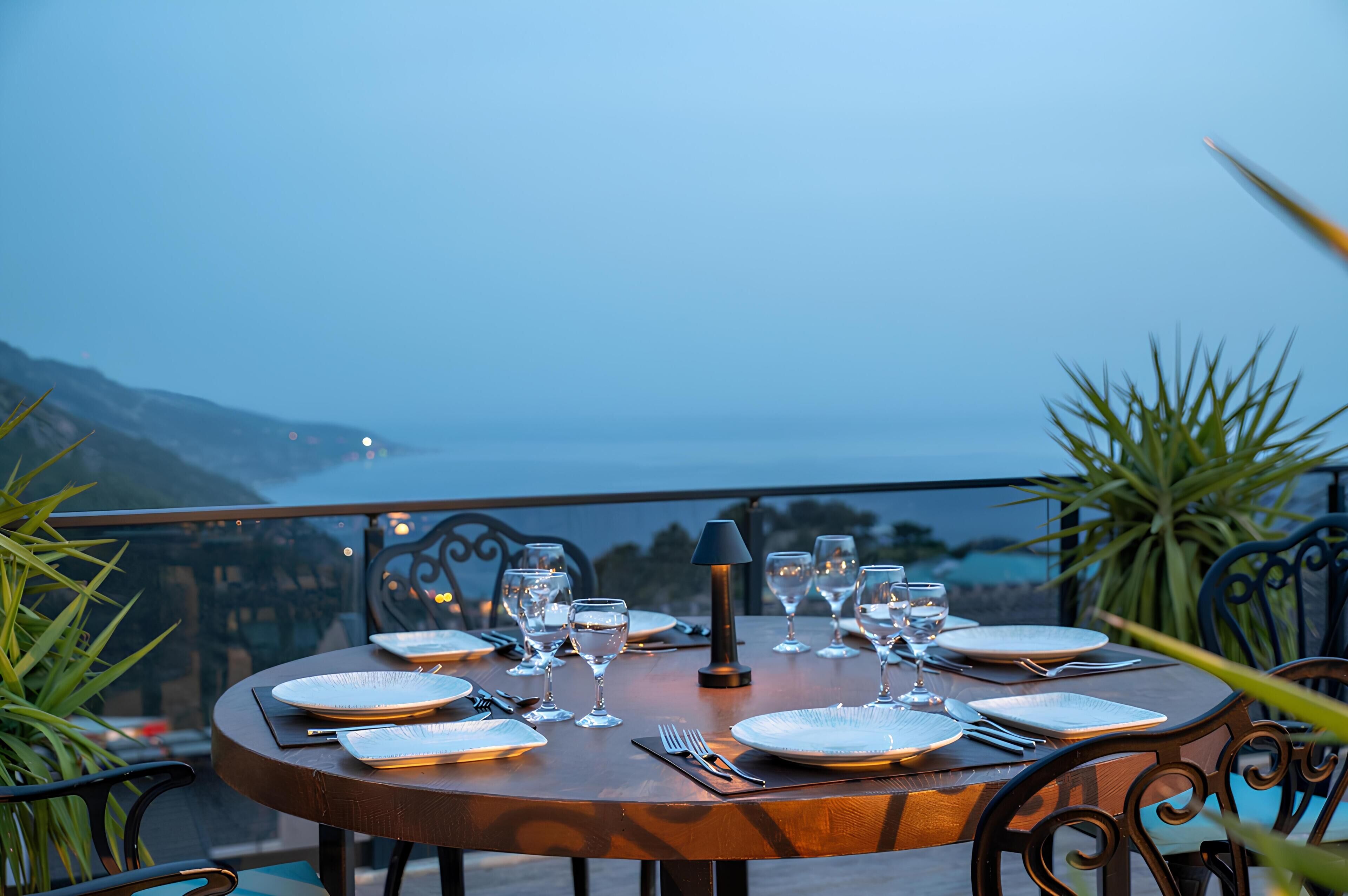 A table set for dinner with a view of the sea and mountains.