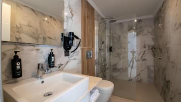 A modern bathroom with a marble wall, a large white sink, a toilet, and a glass-enclosed shower area.