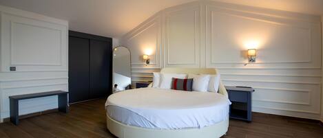 A large round bed with white bedding, two bedside tables, and wall-mounted lamps.