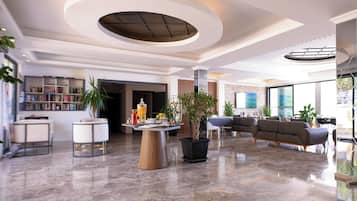 A spacious lobby with a modern design, featuring a central seating area, a reception desk, and a large window providing a view of the outdoors.