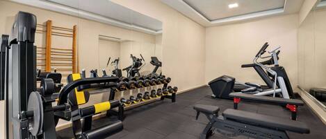 A gym with exercise equipment, a bench, and a rack of dumbbells.