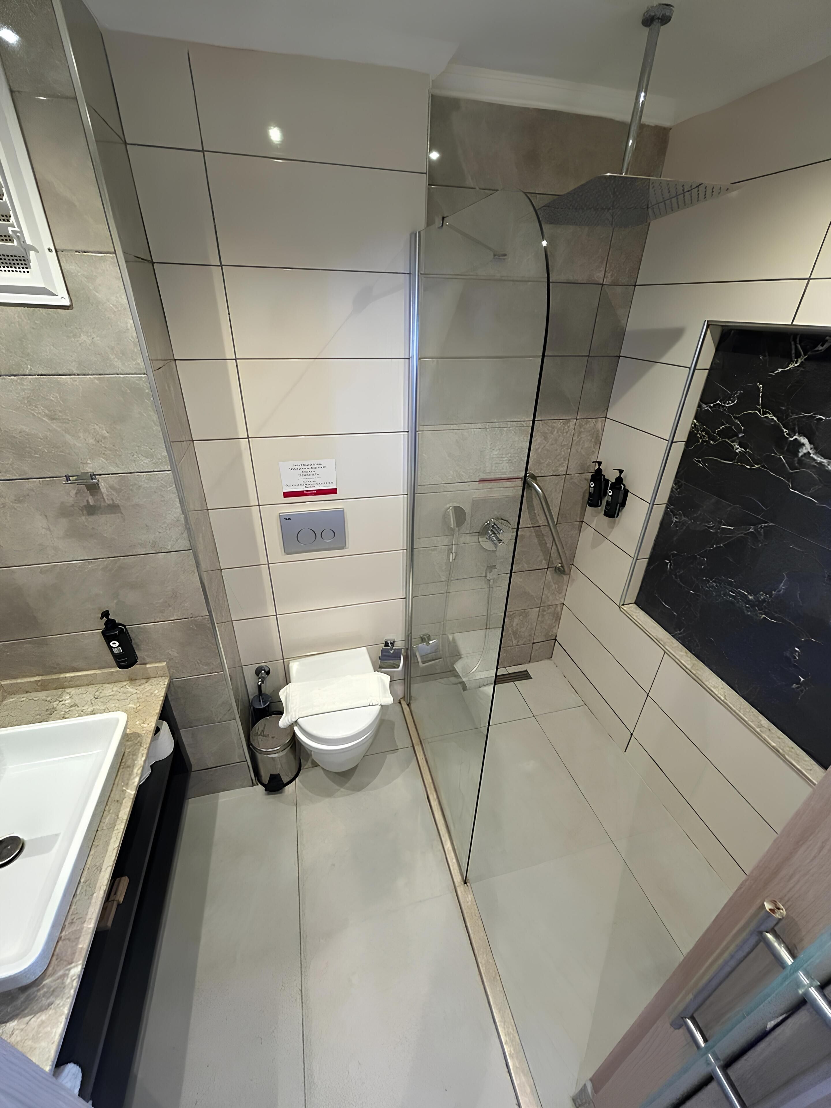 A modern bathroom with a glass-enclosed shower, a white toilet, and a marble-tiled vanity.