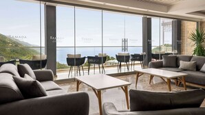A modern hotel lobby with large windows offering a view of the sea and hills. - Ramada by Wyndham Fethiye Oludeniz (Fethiye)