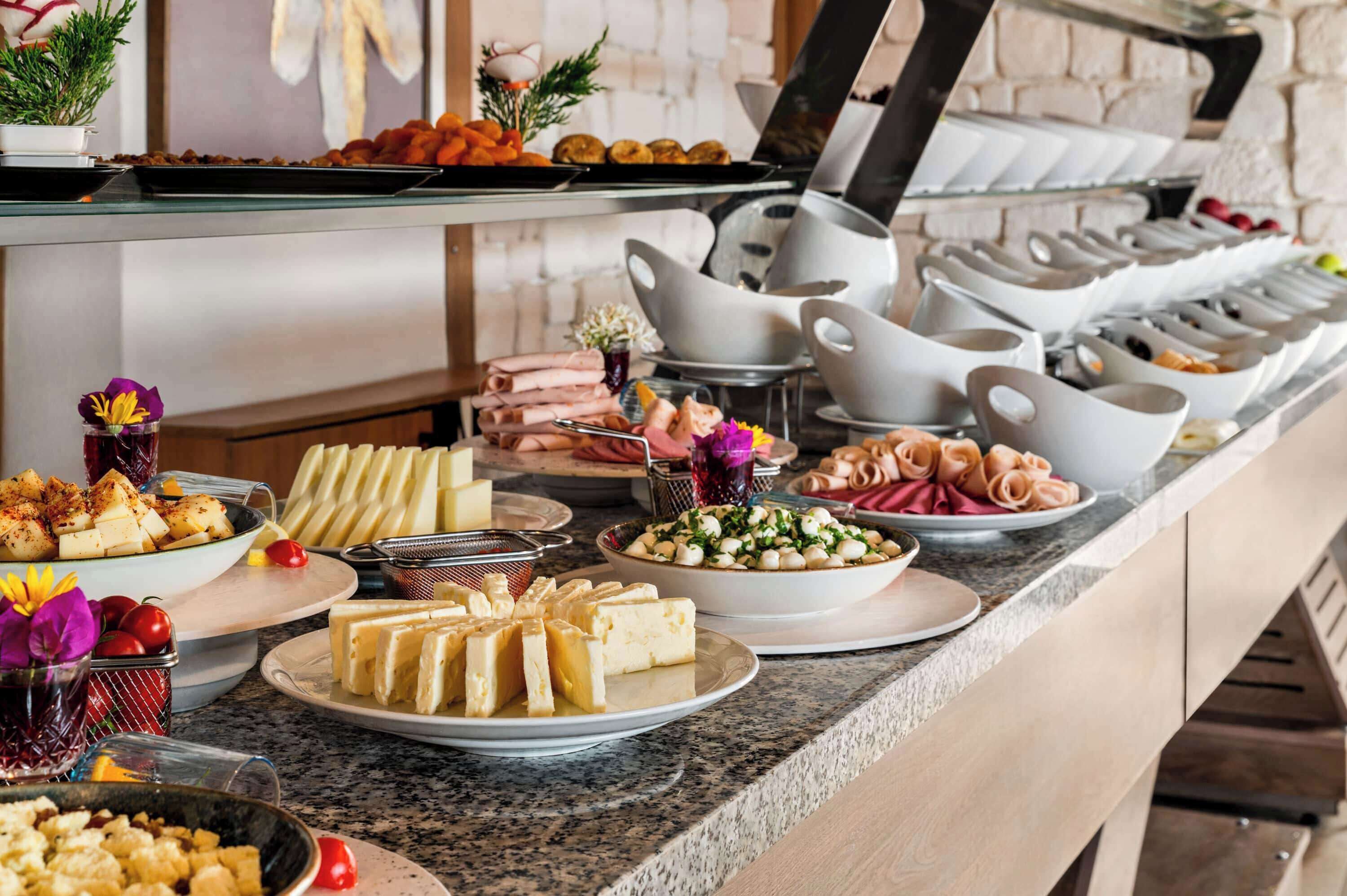A buffet with various food items, including cheeses, meats, and salads.