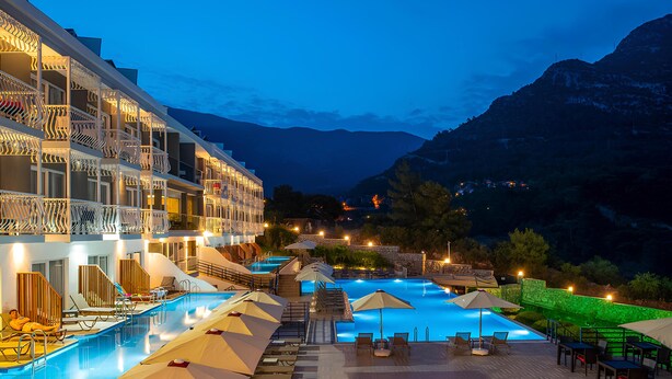 A hotel with a swimming pool, outdoor seating, and mountain views. - Ramada by Wyndham Fethiye Oludeniz (Fethiye)