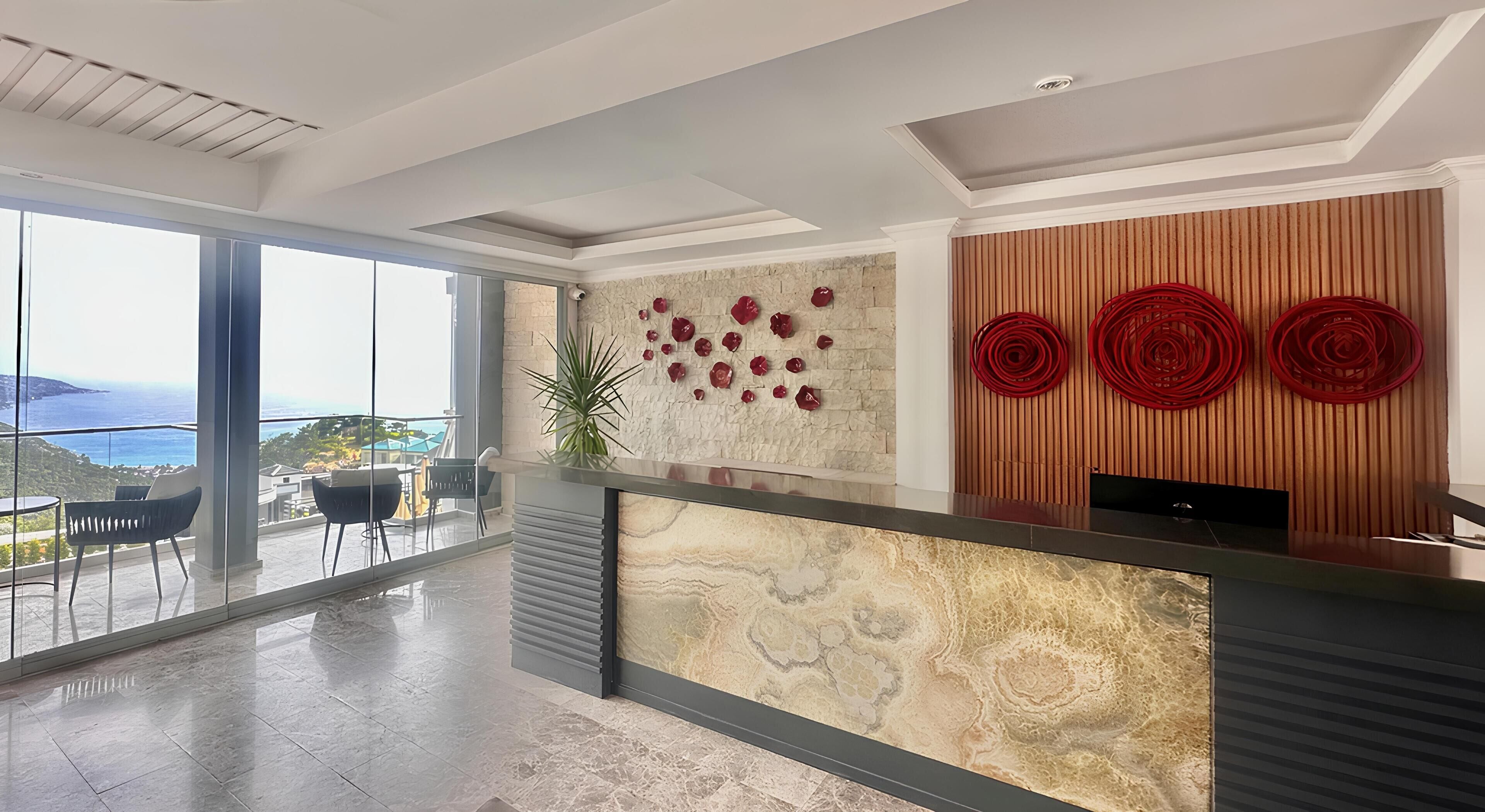 Un área de recepción moderna con mostrador de mármol, un amplio ventanal con vistas al mar y una pared decorativa con círculos rojos.