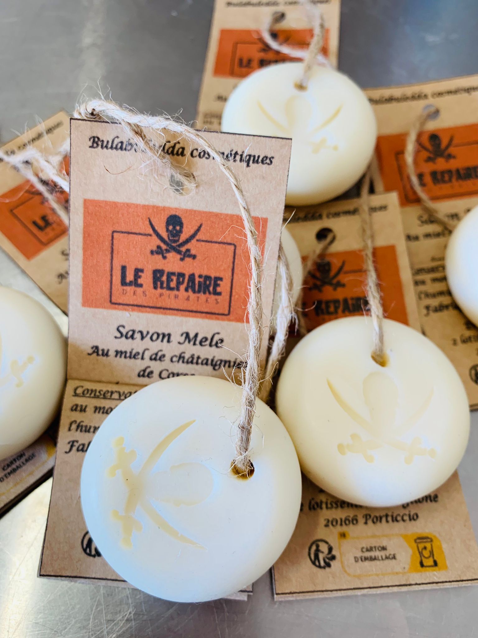 A close-up of white soap bars with a skull and crossbones design, tied with twine and labeled 'LE REPAIRE'.