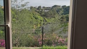 A room with a large window offering a view of a coastal landscape, including greenery and distant hills. - Le Repaire des Pirates (Pietrosella)