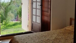 A bedroom with a bed, a ceiling fan, a door leading to a garden, and a view of greenery outside. - Le Repaire des Pirates (Pietrosella)