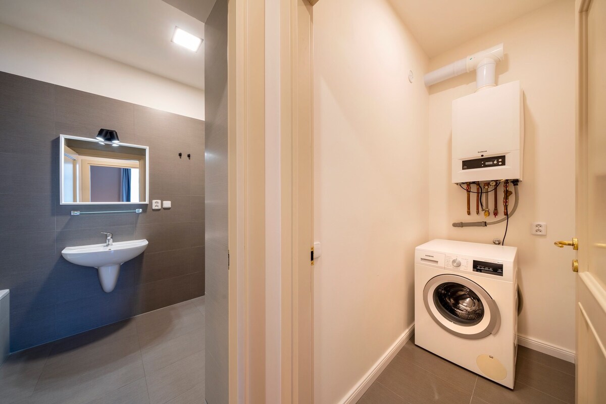 A compact bathroom with a sink, mirror, and a front-loading washing machine.
