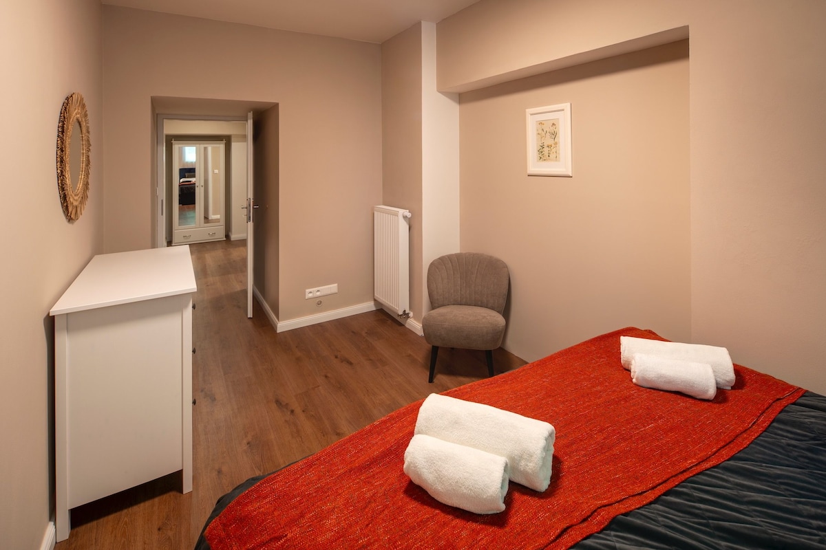 A hotel room with a bed, a chair, a desk, and a radiator.