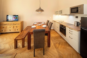 Un comedor con mesa de madera, sillas, televisor y cocina equipada.