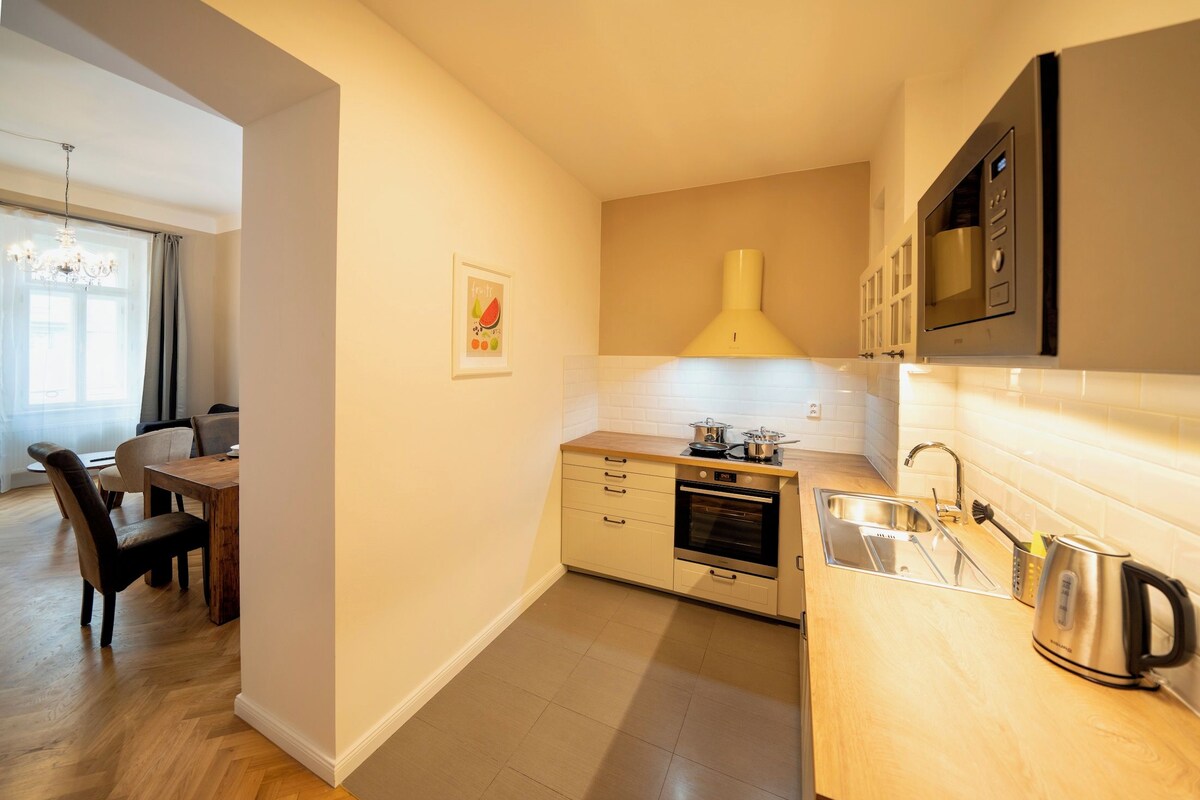 A compact kitchen with a built-in oven, a microwave, and a sink. There is a dining area with chairs and a table visible in the background.