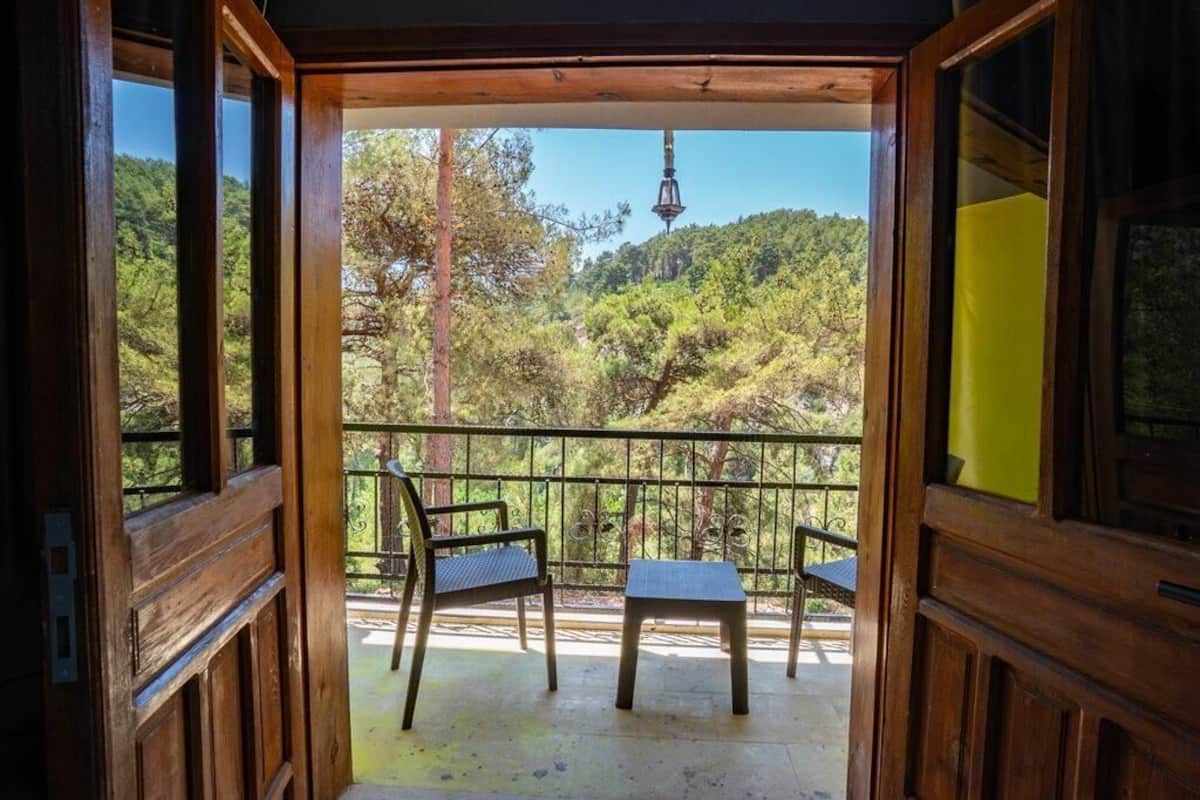 A wooden balcony with a table and chairs, overlooking a forested hillside.