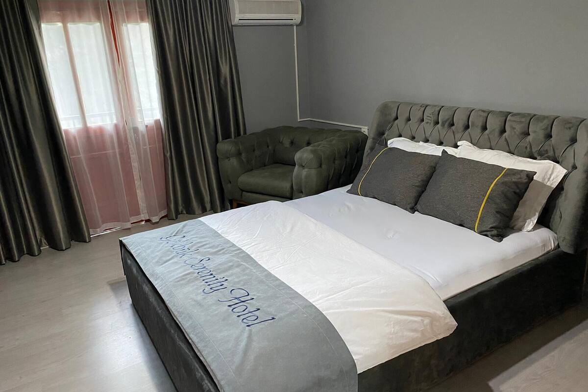 A hotel room with a bed, a green armchair, and a window with curtains.