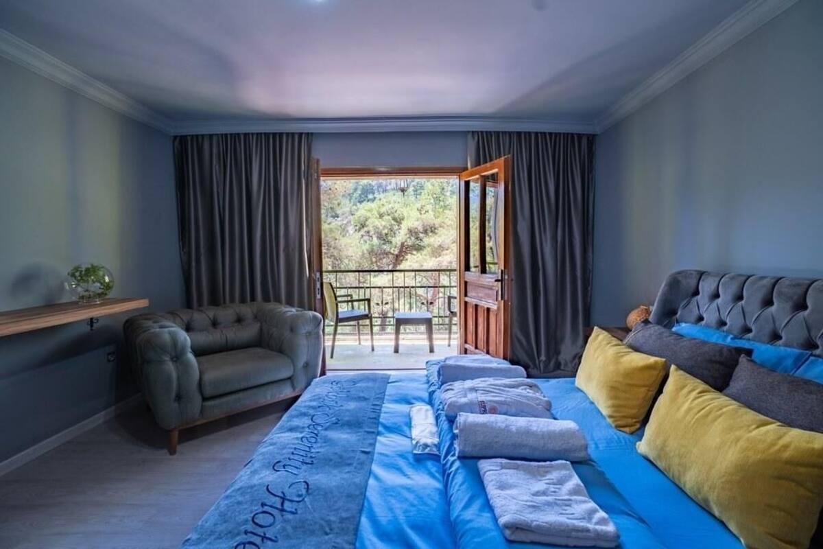 A bedroom with a bed, a sofa, a small table, and a balcony with a view of trees.