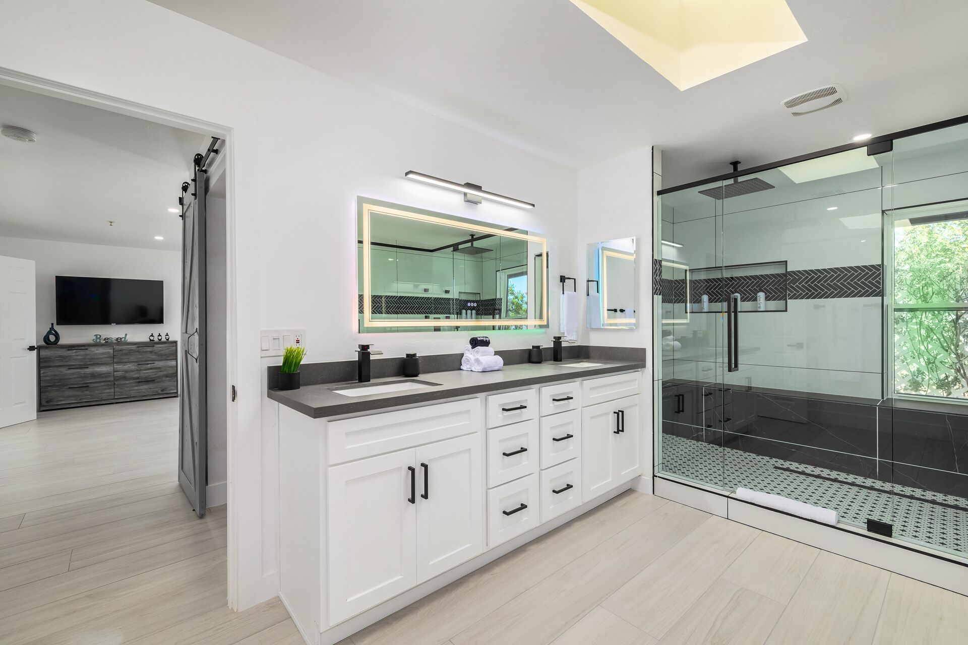 A modern bathroom with a glass shower enclosure, a large mirror, and a vanity with a sink.