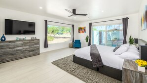 Ein modernes Schlafzimmer mit einem großen Bett, einem Flachbildfernseher, einem Deckenventilator und Blick ins Freie.