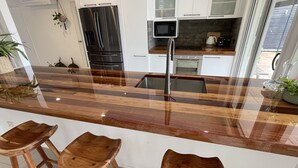 A modern kitchen with a large island, bar stools, a microwave, and a refrigerator. - River front property, huge yard and pool, 2km from the beach.  (Mermaid Waters)