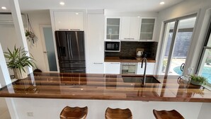 A modern kitchen with a wooden countertop, stainless steel appliances, and three wooden stools. - River front property, huge yard and pool, 2km from the beach.  (Mermaid Waters)