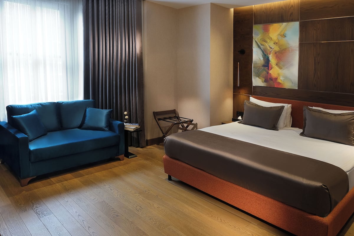 A hotel room with a large bed, a blue sofa, and a wooden floor.