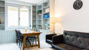 Un salon moderne comprenant un coin repas, un canapé en cuir noir, une table à manger en bois avec des chaises, et des étagères intégrées où sont exposés divers objets.