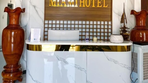 Un comptoir d’accueil avec un plateau en marbre et un panneau en bois portant l’inscription « MIAMI HOTEL ».