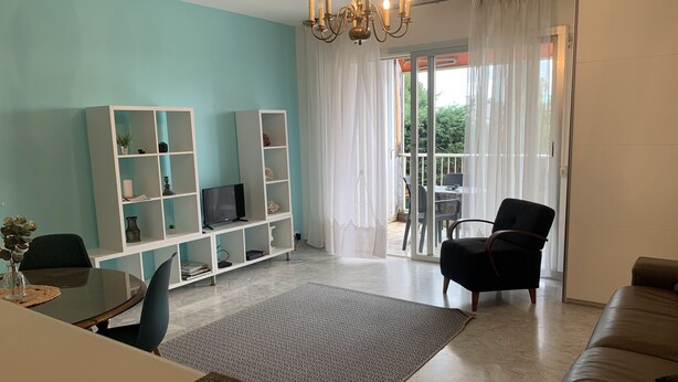 A living room with a sofa, a TV on a white shelf, a dining table with chairs, and a balcony with a chair. - Beau Studio à Antibes (Antibes)