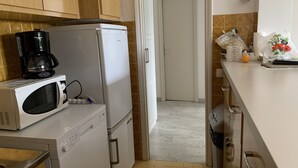 A compact kitchen with a microwave, coffee maker, and refrigerator. There is a tiled backsplash and a door leading to another room. - Logement Entier : Appartement - Antibes, France (Antibes)