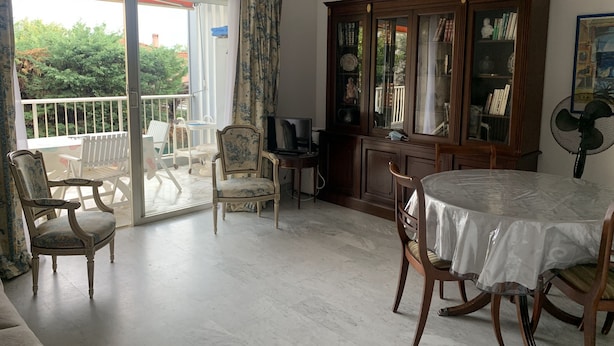 A spacious living room with a large sliding glass door leading to a balcony, a wooden cabinet with glass doors, and a dining table with chairs. - Logement Entier : Appartement - Antibes, France (Antibes)