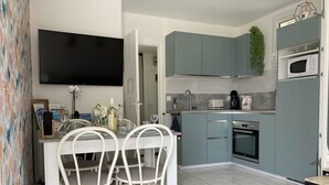A modern kitchen with teal cabinets, a built-in oven, and a microwave. There is a dining area with white chairs and a table.