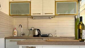 A modern kitchen with wooden cabinets, a built-in oven, and a countertop with a kettle and bottles. - Lamada One Bedroom Apartment (Budva)