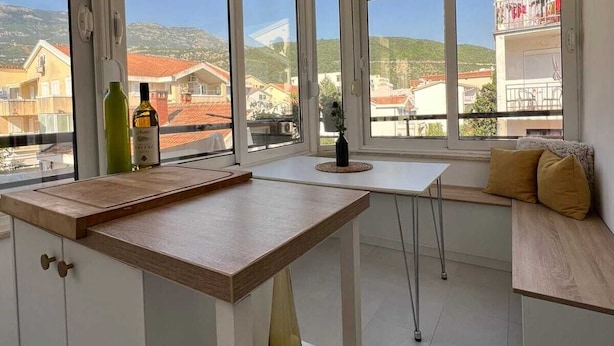 A modern kitchen with large windows, a wooden countertop, and a view of buildings and hills. - Lamada One Bedroom Apartment (Budva)