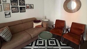 A modern living room with a brown sofa, two red armchairs, a patterned rug, and a unique woven pendant light. - Lamada One Bedroom Apartment (Budva)