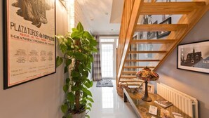 Un couloir avec un escalier en bois, une plante en pot et une table avec des magazines.