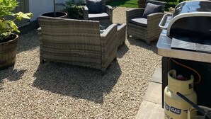 Un espace patio aménagé avec des meubles en osier, un barbecue et une bouteille de gaz.