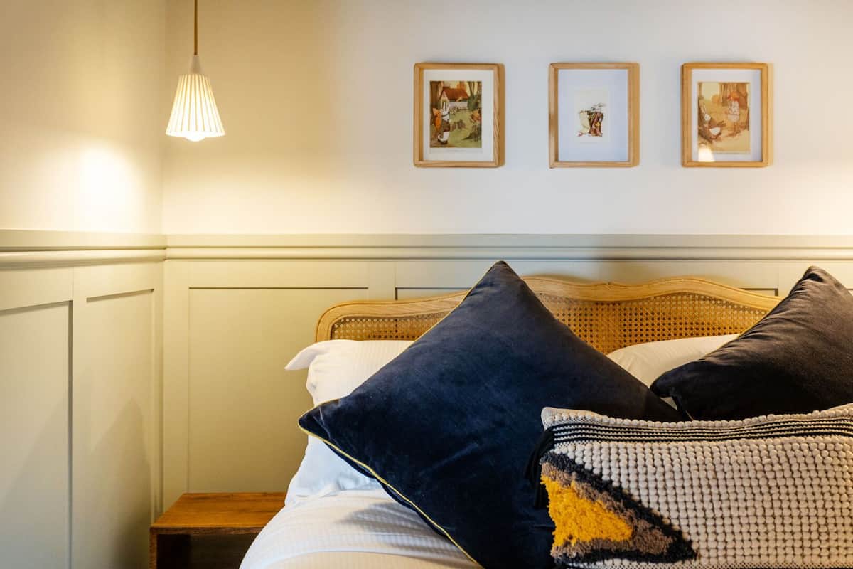 A neatly made bed with a headboard, a bedside table, and three framed pictures on the wall.