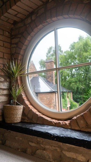 A circular window with a view of a brick building and greenery outside. - The Queen's Chew Magna (Bristol)