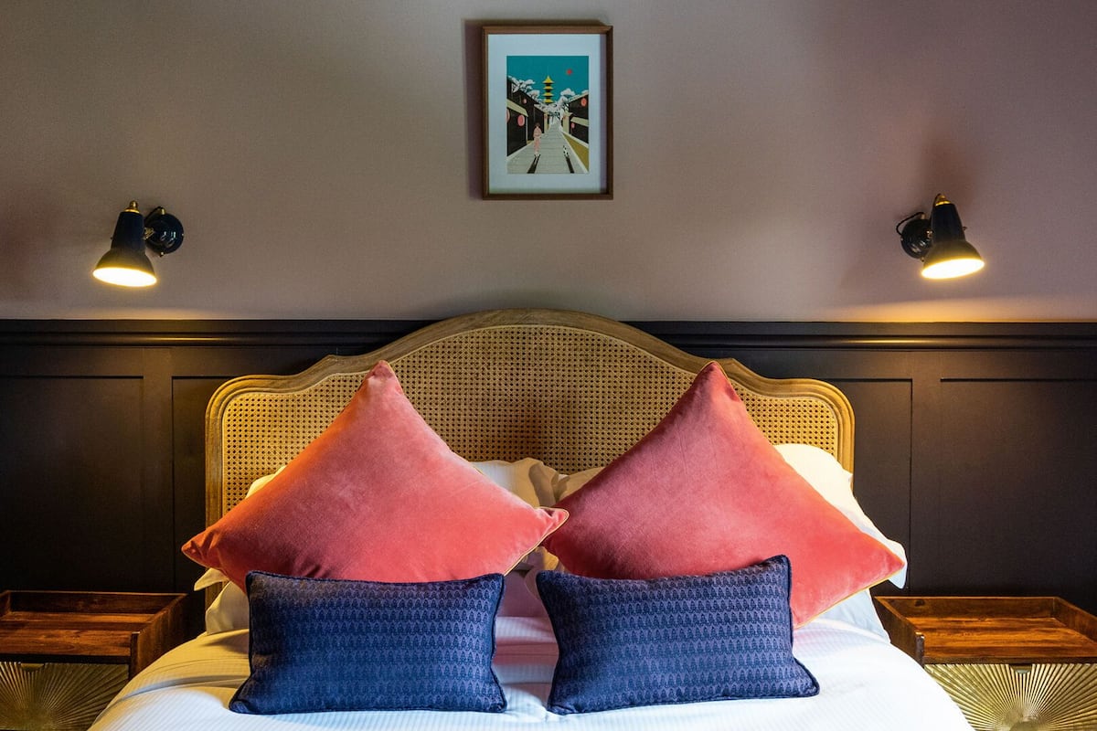 A bed with a rattan headboard, two red and two blue pillows, and two wall-mounted lamps.